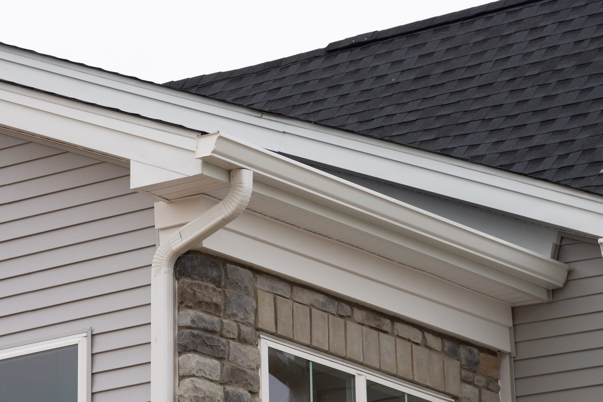 White seamless gutter and downspout on a home with stone accents